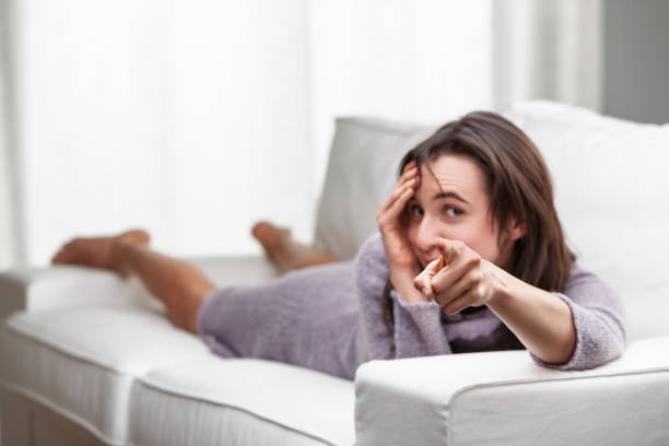 istock Woman lying on couch pointing finger and making funny face 2180797924