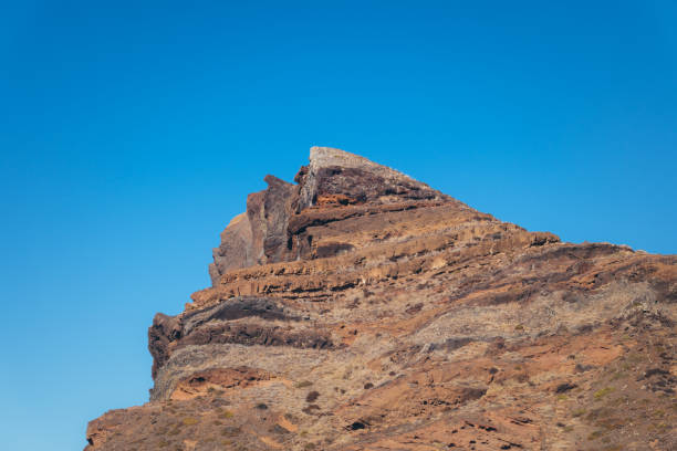 A majestic rock formation stands tall against a vibrant blue sky, showcasing the rugged beauty of nature. The layered strata reveal a rich geological history, while the sharp edges and contrasting colors create a striking visual.