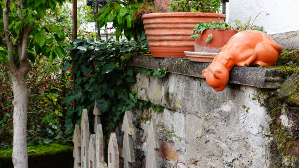 istock A Whimsical Orange Cat Sculpture Resting on a Stone Wall in a Garden Setting 2180799105
