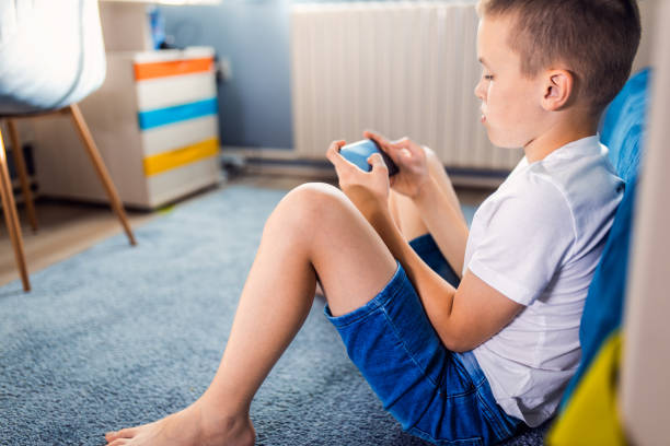 istock Boy playing video game on smartphone sitting on floor in his room. 2180802367