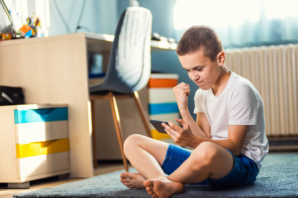 istock Boy playing video game on smartphone sitting on floor in his room. 2180802378