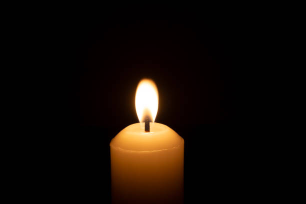 istock A single burning candle flame or light glowing on a big white candle isolated on red or dark background on table in church for Christmas, funeral or memorial service 2180807042