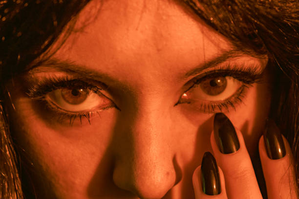 A close-up shot of a witch's face as she raises her long, sharp black nails toward her face. The intense stare and eerie lighting create a mysterious and spooky Halloween atmosphere