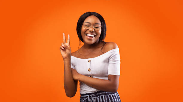 istock Positive Black Girl Gesturing V-Sign Standing On Orange Studio Background 2180816245