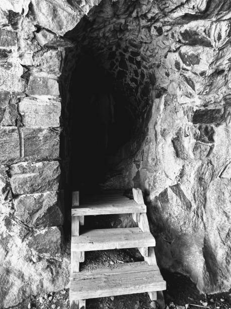 istock A mysterious cave entrance with worn wooden steps leading into darkness, with a barely visible silhouette adding an eerie Halloween vibe 2180830706