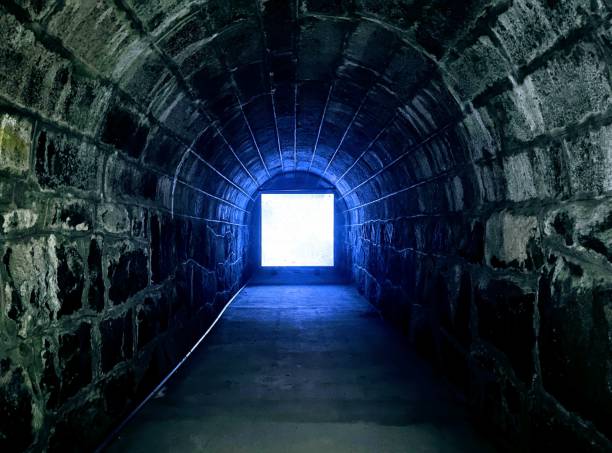A dimly lit stone tunnel with a mysterious blue glow at the end, creating a chilling Halloween ambiance
