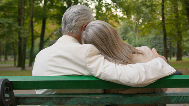 An elderly couple loving each other. They are sitting on a bench. Natural background. Summer and blooming garden