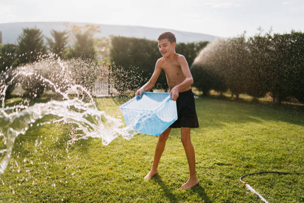 Children having so much fun in the yard spring and splashing with garden hose and refreshing on a hot summer day
