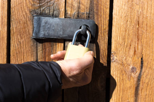 Man's Hand Holding Padlock on Door; Locking or Unlocking