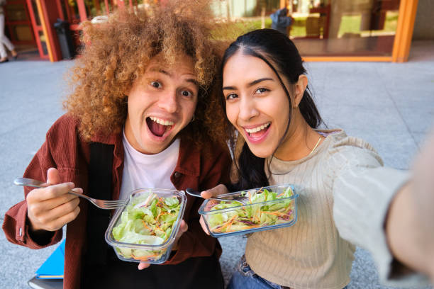 istock Cheerful interracial students eating salad and taking a selfie outside 2180842939