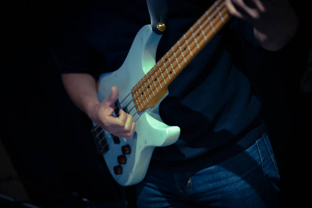 A close-up shot of a musician playing a classic electric bass guitar, showcasing the precision and emotion of their performance. The image highlights the strings and frets in a vibrant, colorful environment.