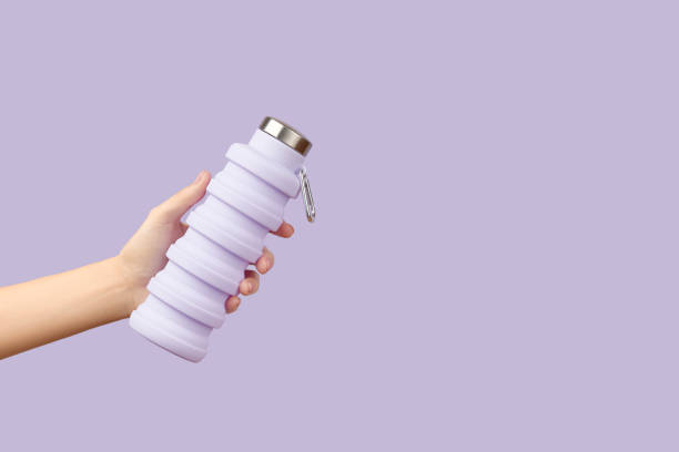 istock Womans hand holding collapsible reusable lilac water bottle on purple background. Zero waste 2180852098