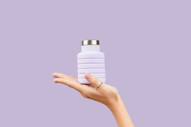 istock Womans hand holding collapsible reusable lilac water bottle on purple background. Zero waste 2180852176