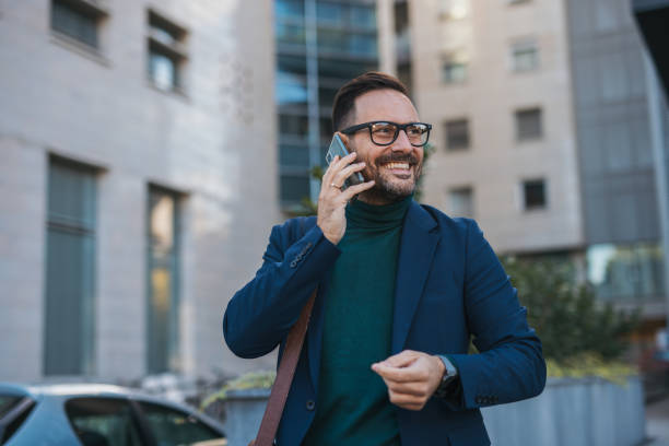 istock business man is having a phone conversation, smiling and well-dressed. In the background, a modern building rises, creating a perfect atmosphere for his successful day. 2180853251