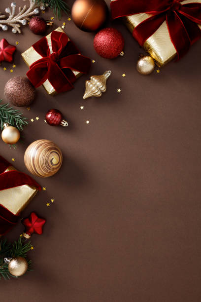 istock Christmas decor layout with gift boxes, golden ribbons, red and gold ornaments, pine branches, and stars on a brown background. 2180859522