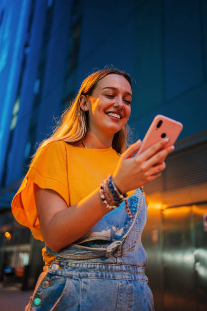 istock Vertical. one happy young girl using her smartphone to browse the internet while walking on the street at night. Female watching the social media with her cellphone. Girl typing on a mobile phone 2180881149