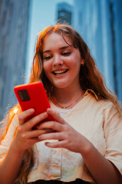 istock Vertical Smiling young woman using a smartphone at night in the city, illuminated by streetlights. Perfect for concepts of technology, communication, social media, or urban life in the evening setting 2180885007