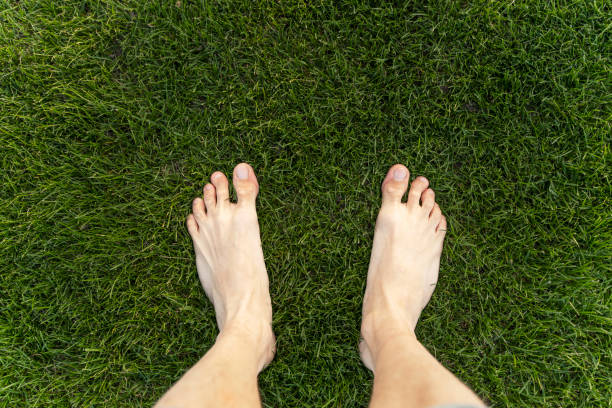 istock Man standing barefoot on green grass lawn texture background 2180892711