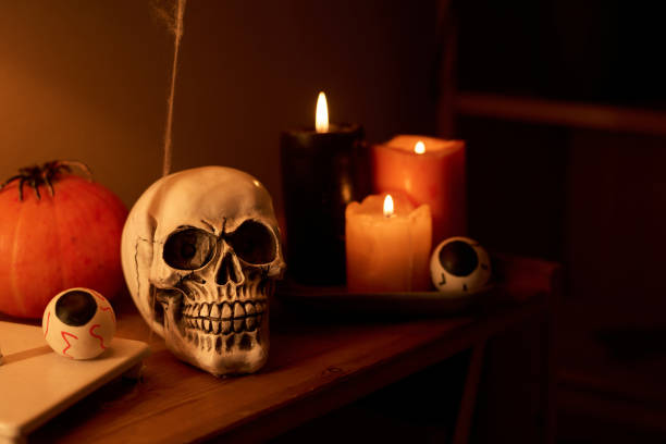 Human skull and eyes, ripe pumpkin with spider and burning candles on shelf in domestic room prepared for Halloween celebration