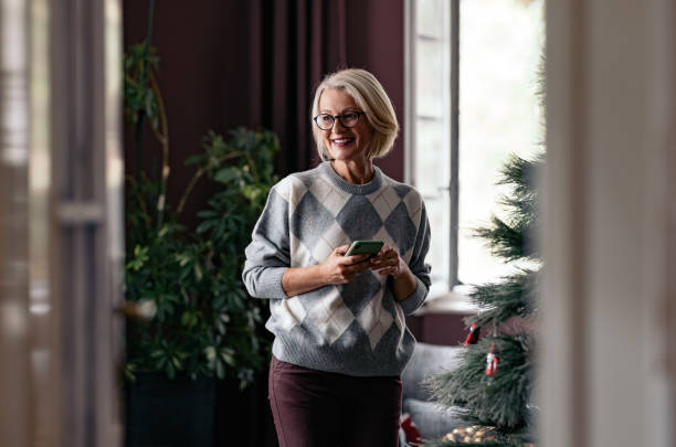 istock Smiling Senior Woman Using Smartphone Near Indoor Christmas Tree 2180894617