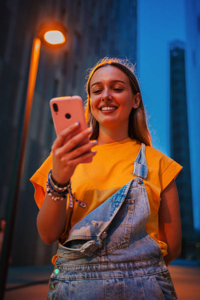 istock Vertical. Real young woman using a cellphone at night. Happy female having fun with a smartphone social media app at dusk. Teenage girl browsing on internet with a mobile phone application at evening 2180894808