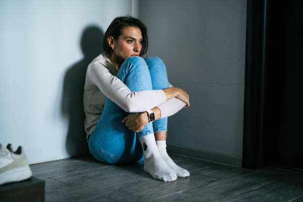 Mid adult female having a mental breakdown at home.She is sitting on the floor feeling lonely and distraught.