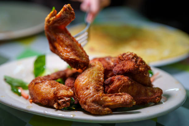 The golden, crunchy coating of the chicken glistens, emphasizing its delicious texture as she lifts it from the plate. The close-up shot highlights the satisfaction of enjoying a classic meal in a cozy dining setting.
