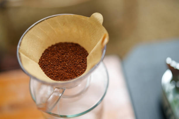 High angle view a clear glass coffee mug sits on a picnic table, with a paper drip bag filled with ground coffee perched above it.