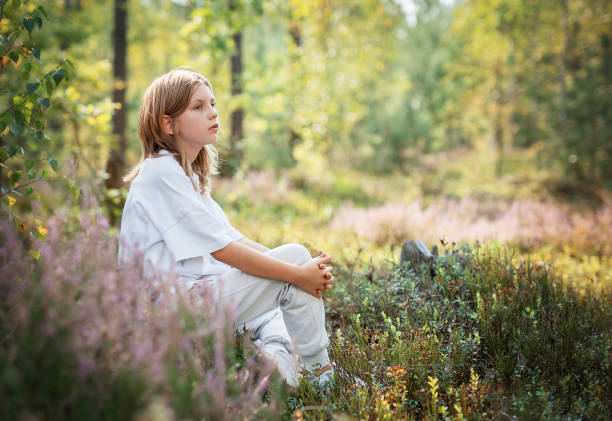 istock A young child sitting quietly in a serene forest, surrounded by vibrant greenery during a sunny afternoon 2180917746