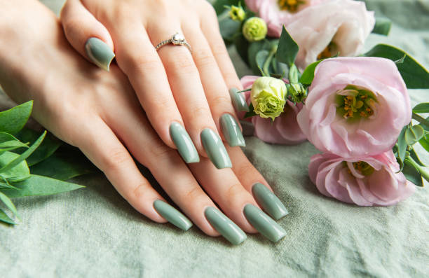 istock Elegant hands with green nail polish resting on a soft fabric surrounded by delicate flowers in a tranquil setting 2180918073
