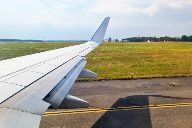 View from an airplane window featuring the wing against a backdrop of a runway and vast countryside. the image serene atmosphere of a clear day, blending technology and nature during flight.