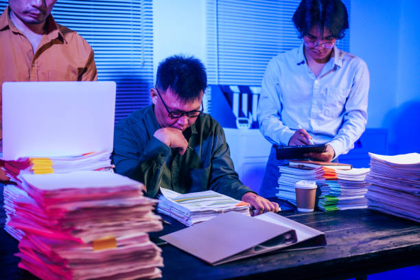 Three men work overtime at night, stressed and overloaded with tasks. They are exhausted, checking documents, and discussing plans. Despite their efforts, they struggle to complete the work on time