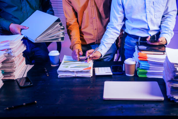 Three men work overtime at night, stressed and overloaded with tasks. They are exhausted, checking documents, and discussing plans. Despite their efforts, they struggle to complete the work on time