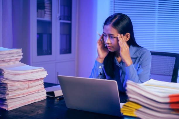 istock An Asian woman works late at night in the office, busy and stressed while checking documents at her desk. She looks tired, managing a heavy workload and feeling the pressure of deadlines 2180923148