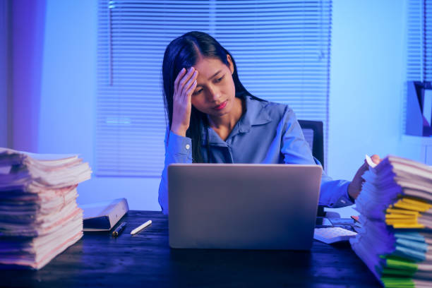 istock An Asian woman works late at night in the office, busy and stressed while checking documents at her desk. She looks tired, managing a heavy workload and feeling the pressure of deadlines 2180923156