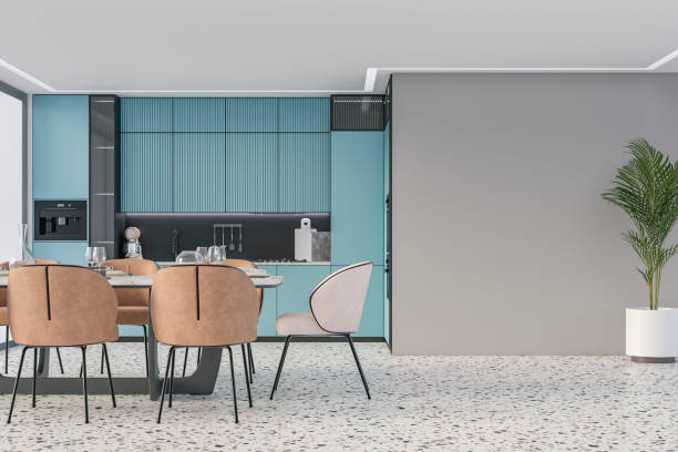istock Modern light blue kitchen with a full dining table, and beige and camel brown leather chairs; a potted plant in front of an empty light gray wall with copy space, on terrazzo floor, a large window on a side 2180926361