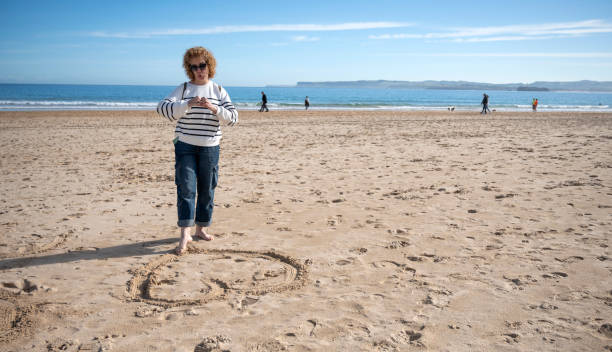 istock Woman creating a heart shape in the sand during a beach walk 2180930158