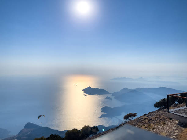 A paraglider gracefully glides above a stunning coastal panorama as the sun sets, casting a golden hue on the sea and islands below.