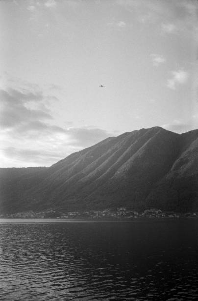 A tranquil scene of a mountain range reflected in a calm lake, captured in black and white at Lake Como. The serene composition evokes peace and a sense of timelessness. Analog photograph on 35mm black and white film, with grain and dust.