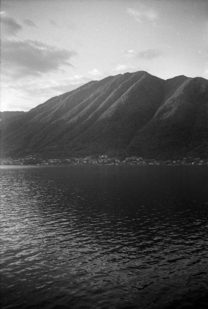 A tranquil scene of a mountain range reflected in a calm lake, captured in black and white at Lake Como. The serene composition evokes peace and a sense of timelessness. Analog photograph on 35mm black and white film, with grain and dust.