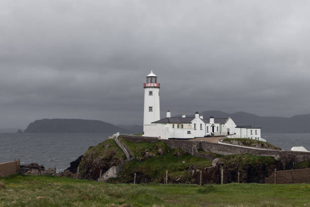 This image captures the remote and scenic St. John’s Point in County Donegal, located along the Wild Atlantic Way in northwestern Ireland. The view showcases the peninsula's lighthouse, an important maritime navigational aid built in the 1830s, surrounded by a stone enclosure and perched above rugged cliffs. The crystal-clear Atlantic waters and the jagged geology of the coastline emphasize the raw beauty of Ireland’s natural heritage. In the distance, the Derryveagh Mountains enhance the sense of remoteness and serenity. This landscape is ideal for travel-related visuals, nature documentaries, and editorial uses reflecting coastal life, exploration, and seafaring traditions.