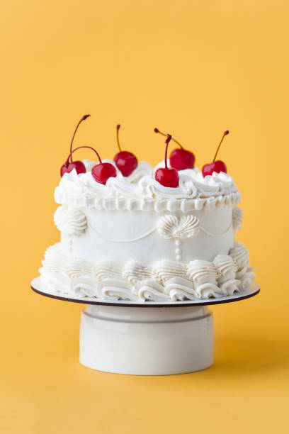 istock Delicate lambeth style birthday cake with white cream cheese frosting decorated with cocktail cherries on the yellow background 2180946330