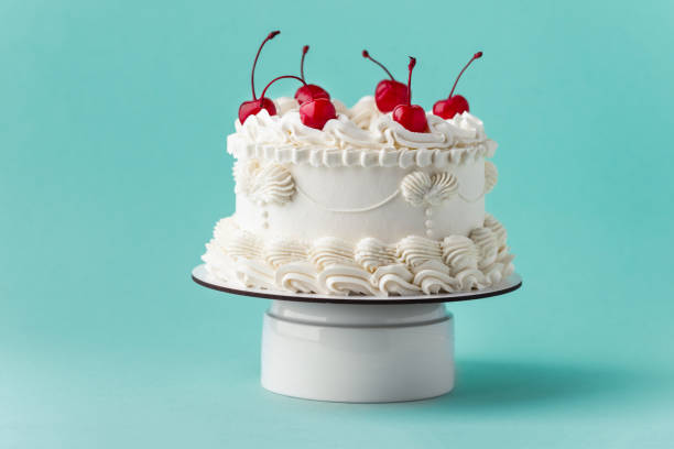 Delicate lambeth style birthday cake with white cream cheese frosting decorated with cocktail cherries on the turquoise background