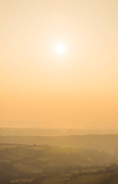 Golden dawn sun illuminating the misty valleys and patchwork quilt landscape of rolling hills and farm fields, rural meadows and headgerows in this tranquil bucolic panoramic vista.