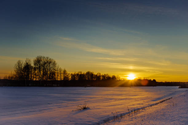 A beautiful sunset over a field of snow. The sky is a mix of blue and orange, with the sun shining brightly in the background. The scene is peaceful and serene, with the snow-covered ground