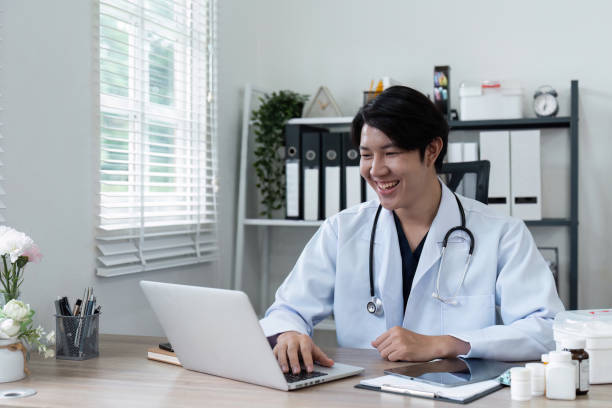 istock Smiling Doctor Working on Laptop in Modern Office with Medical Equipment and Documents 2180950755