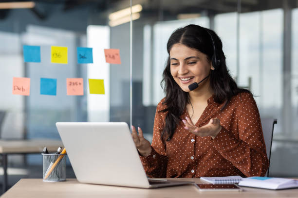 istock Smiling woman wearing headset working on laptop during virtual meeting in modern office setting 2180954325