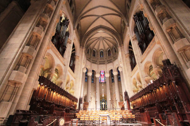 This captivating photograph showcases the breathtaking interior of a cathedral, highlighting the impressive architecture and intricate details of its design. The soaring vaulted ceiling draws the eye upward, while the beautifully crafted choir stalls line the nave, inviting contemplation and reflection. The majestic organ, set against the backdrop of stunning stained glass windows, adds to the spiritual atmosphere of the space. Soft lighting enhances the serene ambiance, making this image perfect for articles or publications focused on architecture, spirituality, or cultural heritage. The harmonious blend of stone and wood, combined with the vibrant colors of the stained glass, creates a visually striking representation of this sacred environment.