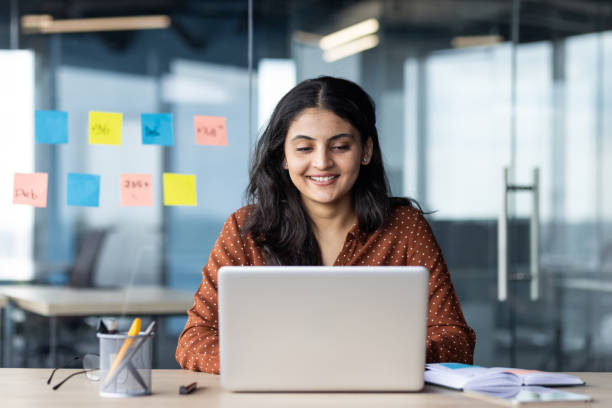 istock Confident woman working on laptop in modern office with colorful sticky notes on glass wall 2180955851