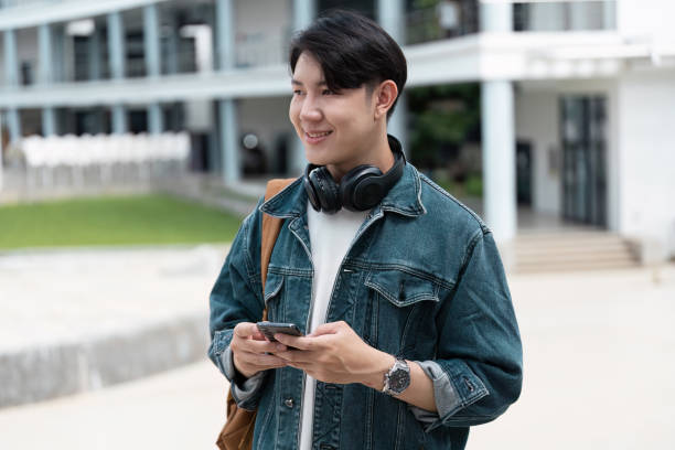 istock Young Student Enjoying Modern Campus Life with mobile and Headphones, Casual Denim Jacket, Outdoor University Setting 2180956981